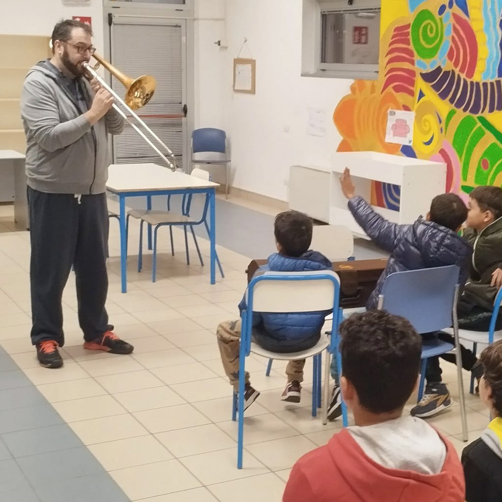 Foto di un signore che suona la tromba a dei bambini
